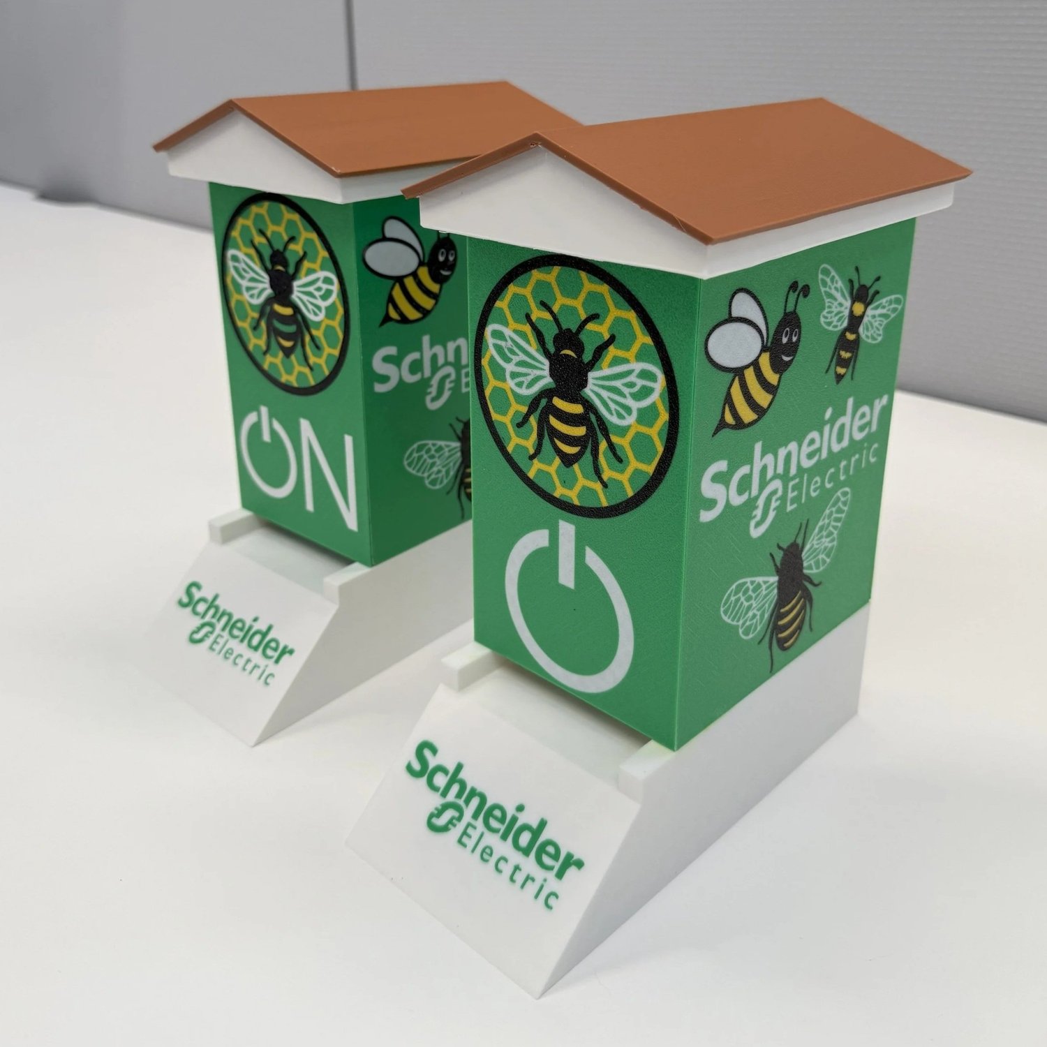 Two 3D printed branded scale-model beehives for Schneider Electric with removable roofs and stands